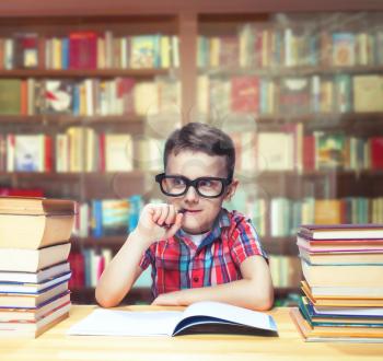 Scientist little child learns homework in the school library. Pupil in glasses against book shelves