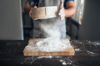 Male baker hands filters the flour through a sieve over cutting board. Bread preparation. Homemade bakery