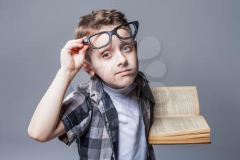 Smart pupil in glasses with textbook in hands, studio photo shoot. Child education concept