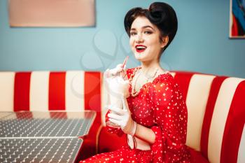 Sexy pin up girl with make-up drinks milkshake through a straw in retro cafe, popular american fashion 50s and 60s