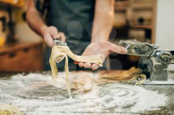 Chef with knife in hand cooking fresh homemade fettuccine in pasta machine on wooden kitchen table