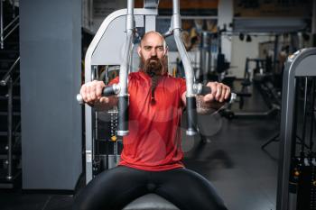 Muscular athlete on exercise machine in gym. Bearded man on workout in sport club