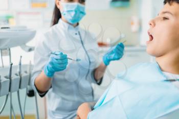Little patient in a dental chair, professional pediatric dentistry, children stomatology, female dentist in mask and gloves on background