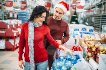 Young couple chooses christmas tree toys in shop, family tradition. December shopping of holiday goods and decorations