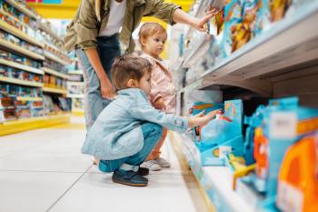 Mother with her little children at the shelf in kids store. Mom with daughter and son choosing toys in supermarket together, family shopping