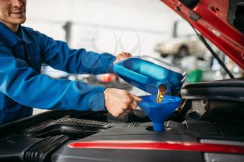Technician pours new oil into the car engine. Vehicle engine maintenance, autoservice