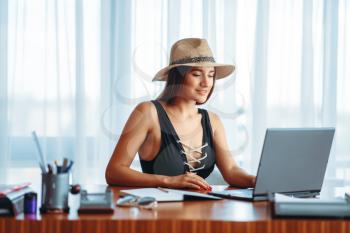 Young woman works on laptop at the table in office and dreaming about a vacation