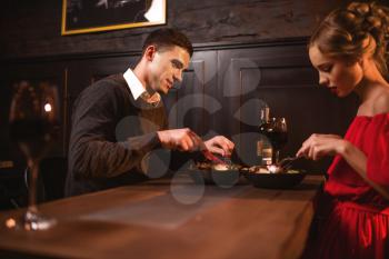 Beautiful love couple eating in restaurant, romantic evening. Elegant woman in red dress and her man leisure together