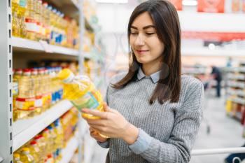 Woman choosing sunflower oil in a supermarket, family shopping. Female customer in shop, buyer in market