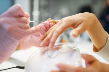 Beautician in pink gloves applying nail varnish to female client, manicure in beauty salon. Manicurist doing hands care cosmetic procedure