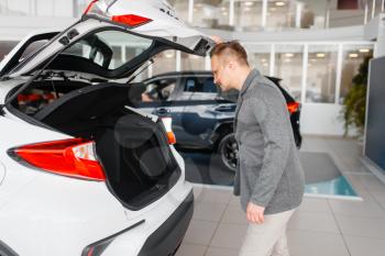 Man looks at the trunk of new car in showroom. Male customer choosing vehicle in dealership, automobile sale