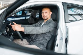 Man sitting in new car, showroom. Male customer choosing vehicle in dealership, automobile sale, auto purchase