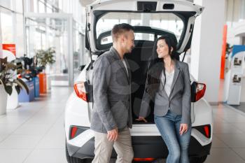 Couple buying new car in showroom, man and woman near the opened trunk. Male and female customers choosing vehicle in dealership, automobile sale, auto purchase