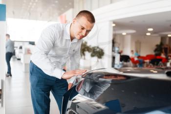 Manager checks the quality of new car paintwork in showroom. Male customer buying vehicle in dealership, automobile sale, auto purchase