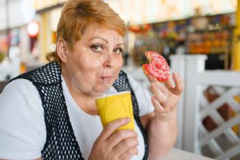 Fat woman eating doughnuts in fastfood restaurant, unhealthy food. Overweight female person at the table with junk dinner, obesity problem