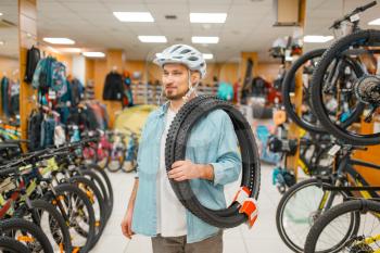 Man in cycling helmet holds bicycle tyres, shopping in sports shop. Summer season extreme lifestyle, active leisure store, customers buying bike equipment