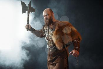 Bearded viking with axe enters the battle, barbarian image. Ancient warrior in smoke on dark background