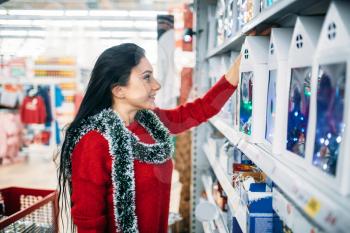 Young woman looks on christmas gifts in supermarket. December shopping, choosing of holiday decorations