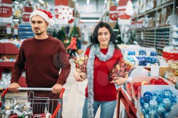 Young couple chose a lot of Christmas toys in shop, family tradition. December shopping of holiday goods and decorations