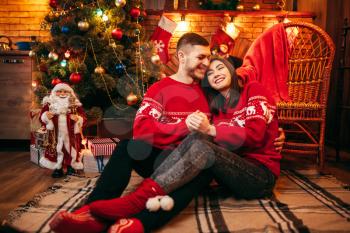 Love couple hugs together, christmas celebration. Xmas holidays, man and woman sitting on the floor, festive decoration on background