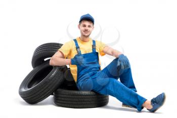 Service worker in blue uniform sitting on car tires, white background, tyre repairman, wheel mounting