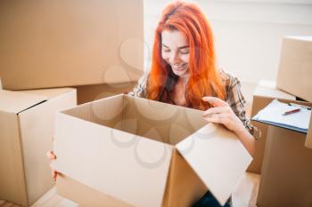 Young woman unpacking cardboard boxes, housewarming. Relocation to new home