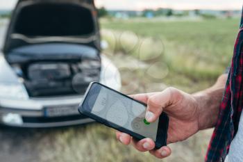 Male person hand with phone, broken car with open hood. Problem with vehicle, emergency service