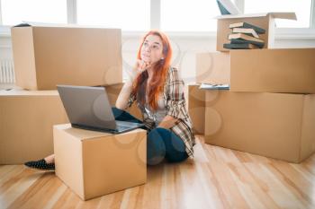Smiling girl using laptop among cardboard boxes, moving to new house, housewarming