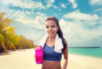 Young woman with sport bottle on seaside. Girl on coastline, fitness workout