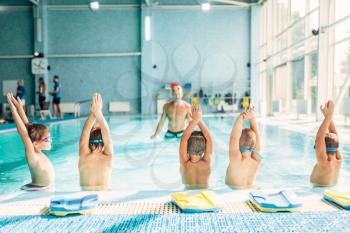 Kids doing exercise in swimming pool with hands up. Instructor shows an exercise for children. Healthy sports activity in pool. Sportive kids activity in modern sport center with pool.