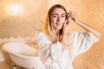 Happy woman in white bathrobe doing makeup in bathroom, facial skincare in bathroom. Bodycare and hygiene, healthcare