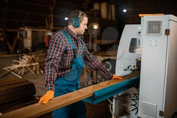 Woodworker in uniform and headphones works on woodworking machine, lumber industry, carpentry. Wood processing on factory