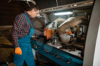 Carpenter in uniform near woodworking machine, lumber industry, carpentry. Wood processing on factory, forest sawing in lumberyard