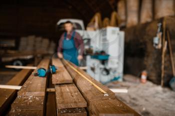 Carpenter with measuring tape measures boards, woodworking machine on background, lumber industry, carpentry. Wood processing on factory, forest sawing in lumberyard