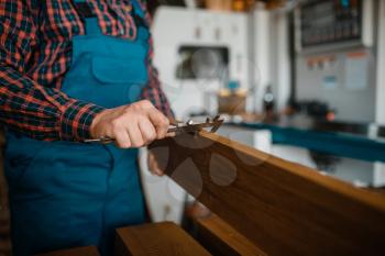 Carpenter in uniform measures the board with caliper, woodworking machine on background, lumber industry, carpentry. Wood processing on factory, forest sawing in lumberyard