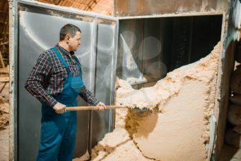 Carpenter with a shovel removes sawdust, woodworking factory, lumber industry, carpentry. Wood processing on factory, forest sawing in lumberyard