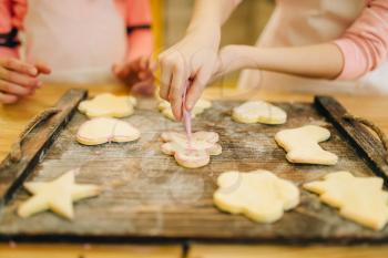 Two little girls cooks spread out cookies on a wooden board, bakery preparation on the kitchen, funny bakers. Kids cooking pastry, children chefs preparing cake