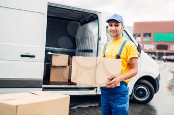 Workman or courier in uniform holds carton box in hands, truck with parcels on background. Distribution business. Cargo delivery. Empty, clear container