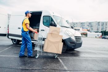 Male courier with parcel trolley against truck with carton boxes. Distribution business. Cargo delivery. Empty, clear containers. Logistic and post service