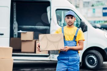 Cargo delivery service, male courier in uniform with box in hand unloads truck with cardboard parcels. Empty container