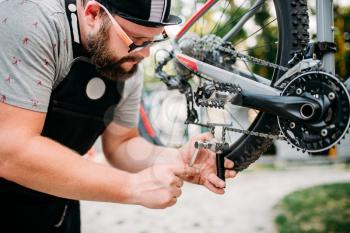 Bicycle mechanic hands adjusts bike chain with service tools. Cycle workshop outdoor. Bicycling sport, bearded repairman