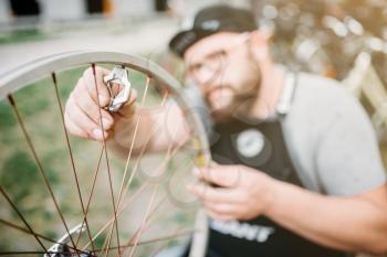 Professional bicycle master in apron adjusts bike spokes and repair wheel with service tools closeup. Cycle workshop outdoor. Bicycling sport, 