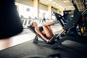 Young woman in sportswear trains on exercise machine in sport gym. Female athlete workout in fitness club