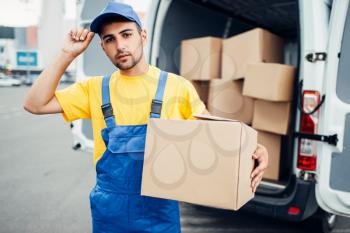 Cargo delivery service, male courier in uniform with box in hand and truck with cardboard parcels. Empty container