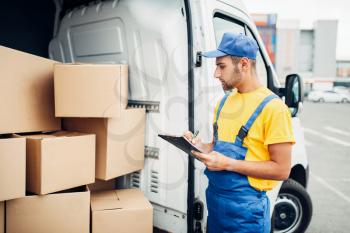 Cargo delivery service, male courier in uniform with box in hand and truck with cardboard parcels. Empty container