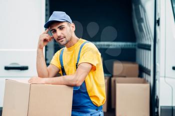 Workman or courier in uniform holds carton box in hands, truck with parcels on background. Distribution business. Cargo delivery. Empty, clear container