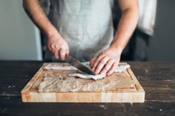 Male chef cuts with knife raw fish slices on wooden cutting board. Seafood cooking. Fresh sea food preparation