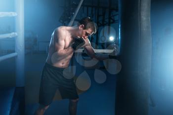 Man in black handwraps exercises with bag in gym. Boxing workout, mens sport