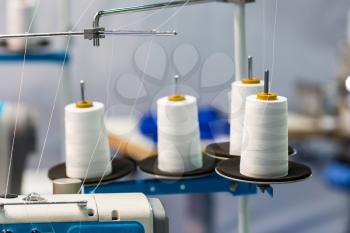 Spools of white threads on sewing machine, closeup. Cloth factory, weaving, textile production, clothing industry