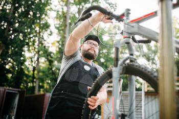 Bicycle mechanic repair bike, top view. Cycle workshop outdoor. Bicycling sport, bearded service man work with wheel